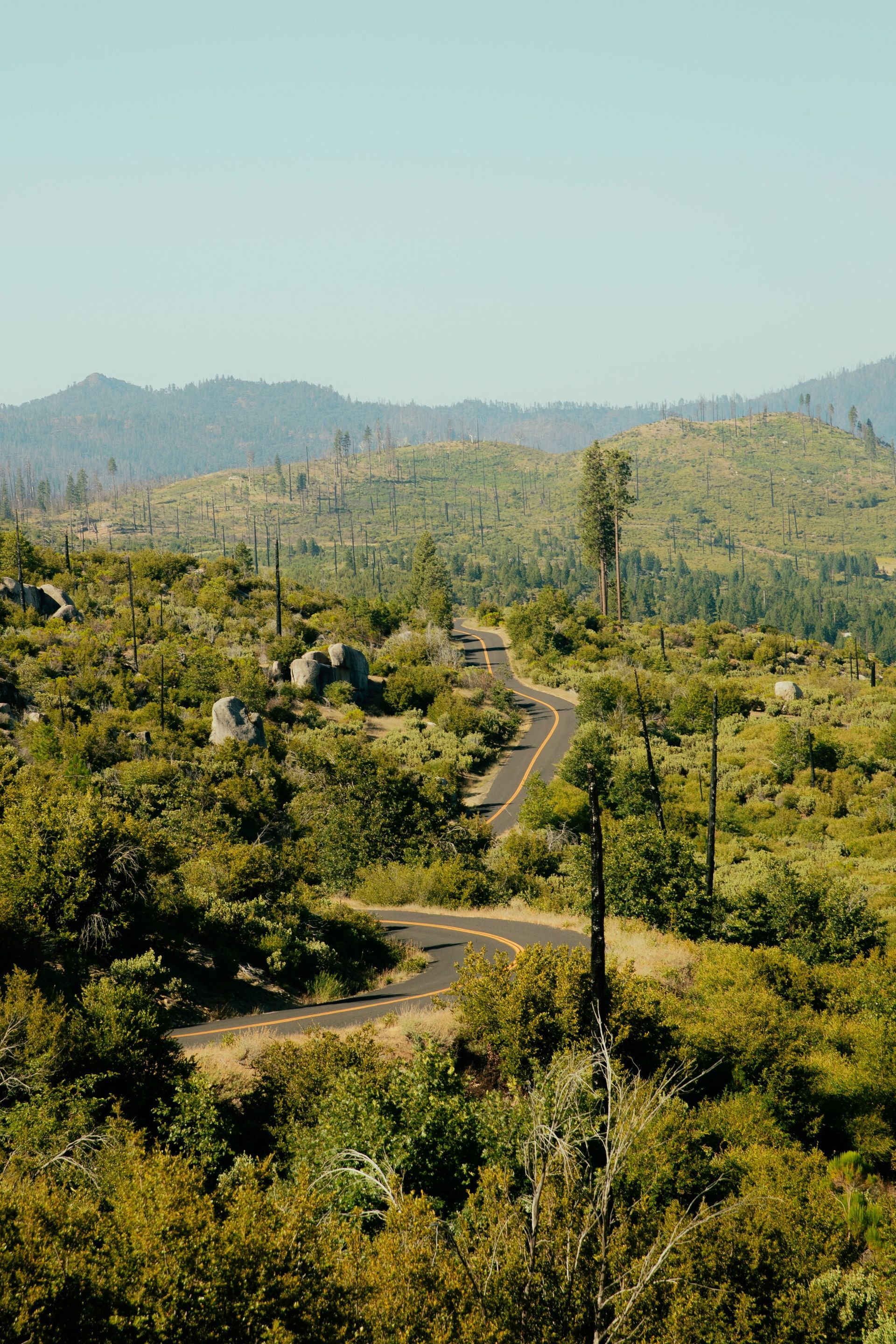 Winding road through a green, mountainous landscape under a clear, blue sky.