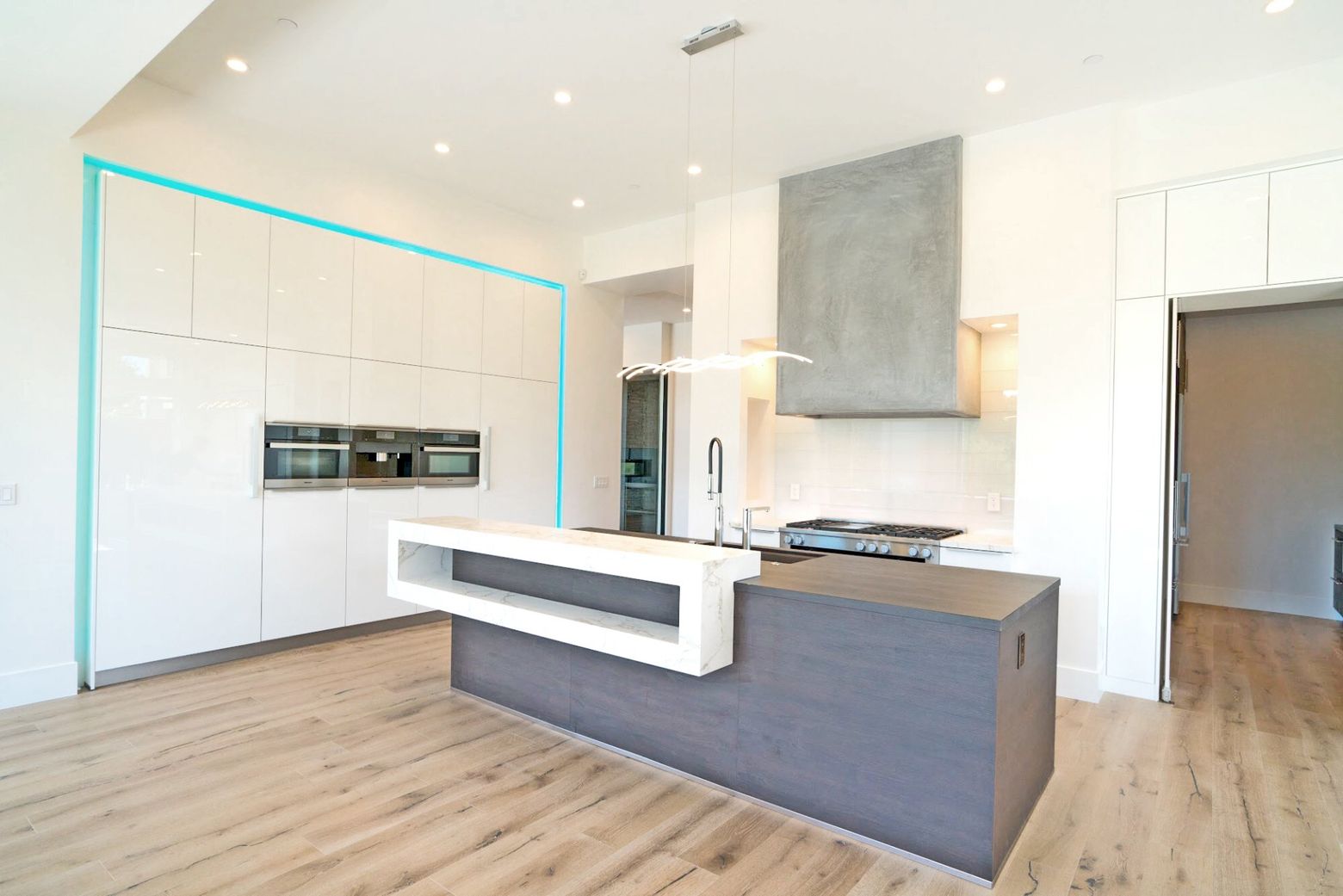 Modern white kitchen with wood floors, gray island, and built-in appliances