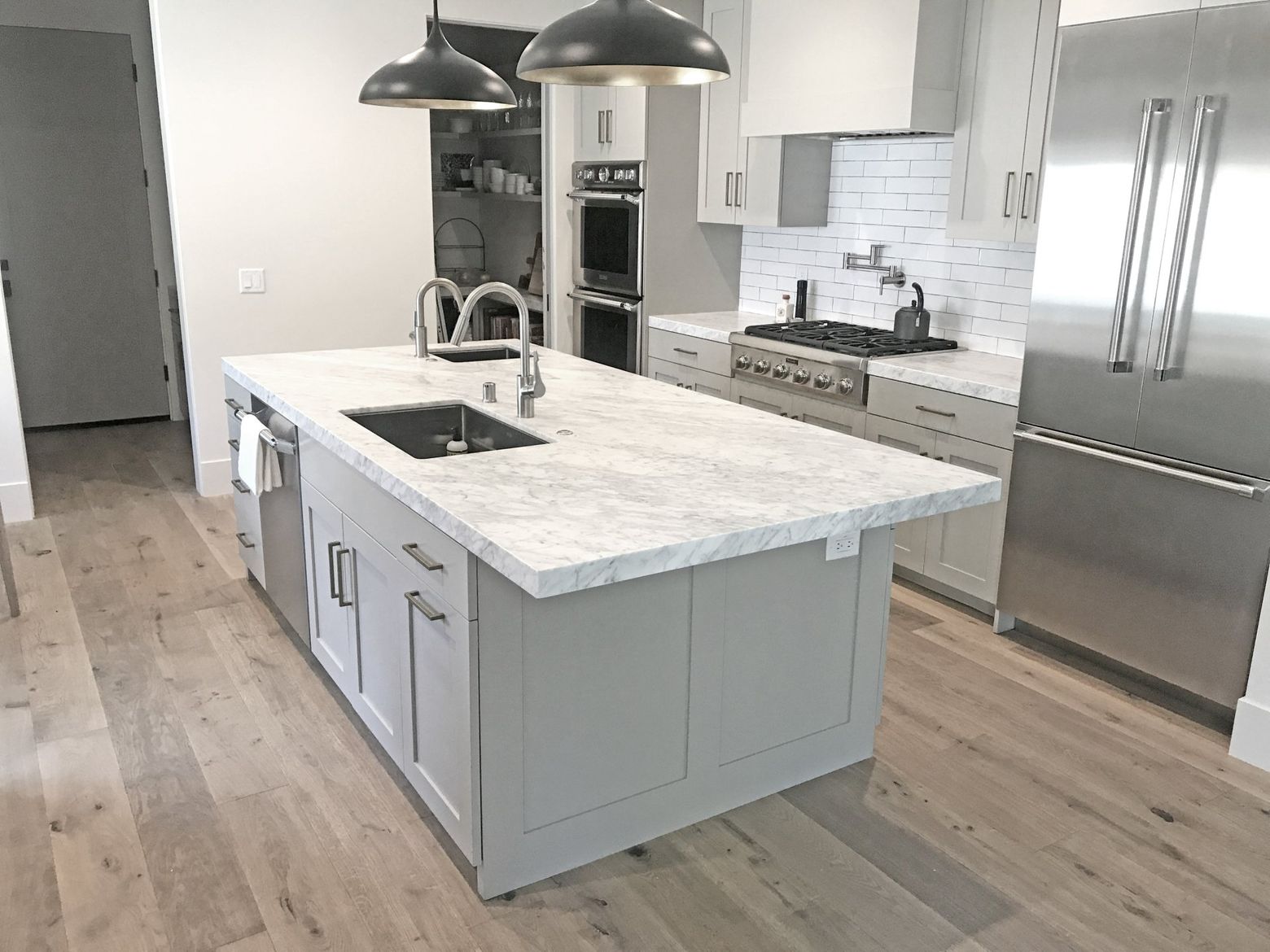 Modern kitchen with large island, pendant lights, stainless steel fridge, and light wood floors