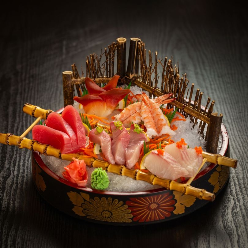 Japanese sashimi platter with assorted fish on a decorative tray, garnished with ginger and wasabi