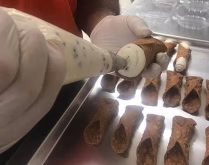 Gloved hands piping filling into a canoli