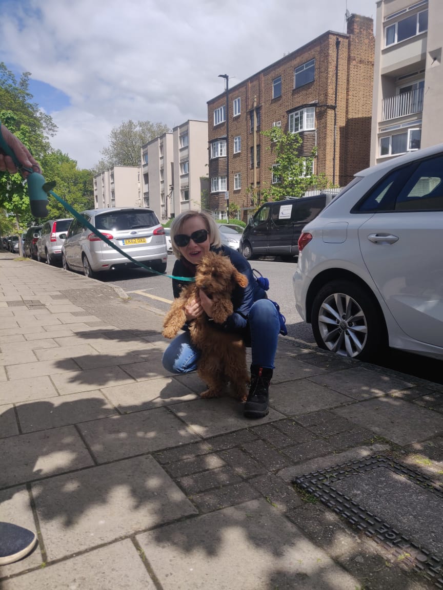 A middle-aged woman crouched on the pavement of a suburban London street, holding up a fluffy puppy.