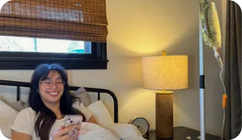 A woman is laying in bed with an iv in her arm and looking at her phone.