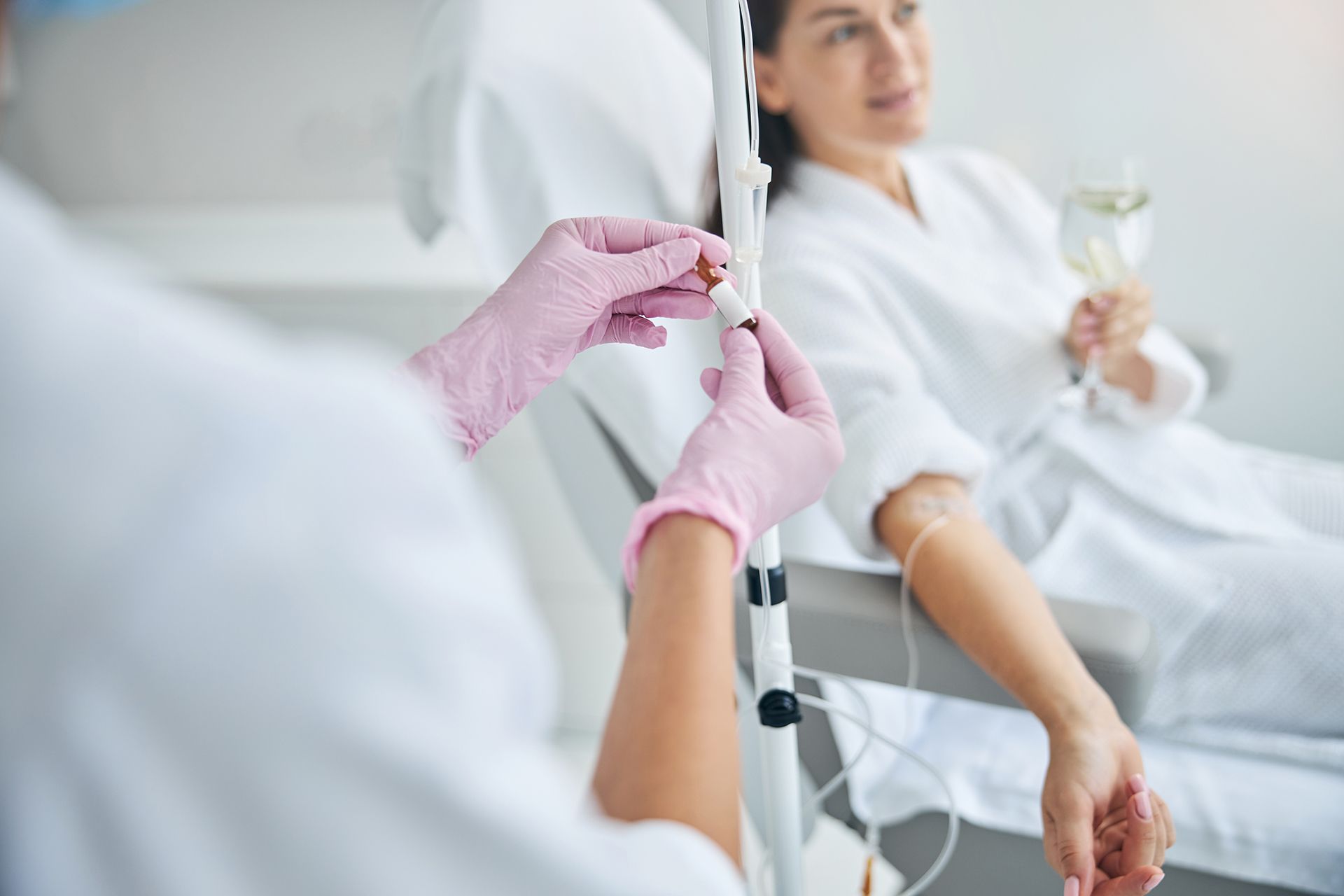 Healthcare worker adjusting an IV line for a patient resting in a hospital bed, wearing pink gloves