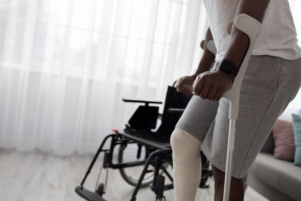 A man with a cast on his leg is standing next to a wheelchair.