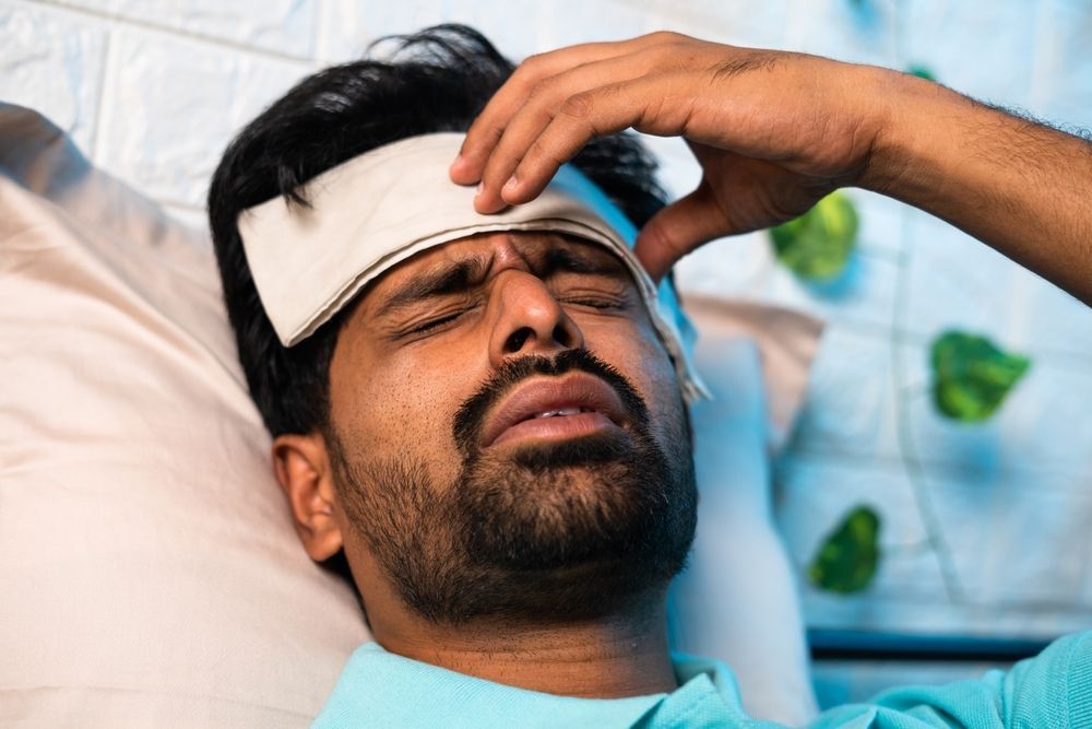 A man is laying in bed with a towel on his forehead.