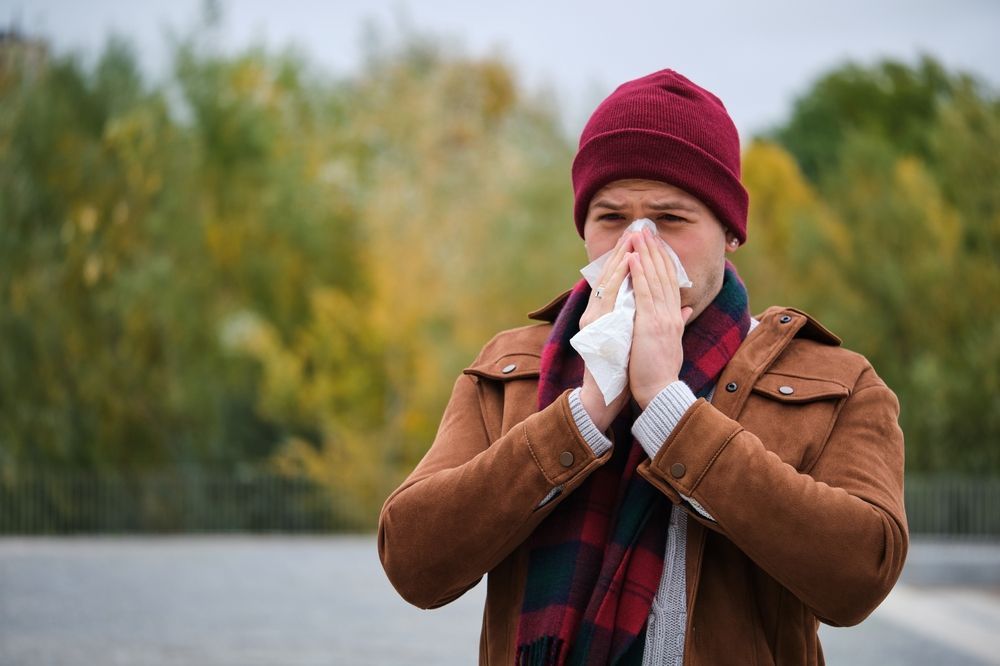 A man in a hat and scarf is blowing his nose into a napkin.