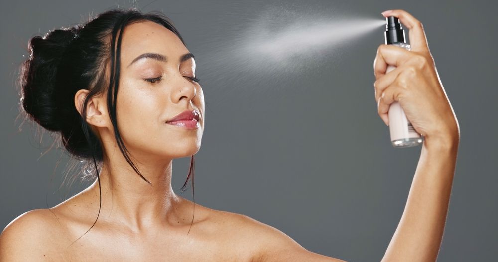 A woman is spraying a spray bottle on her face.