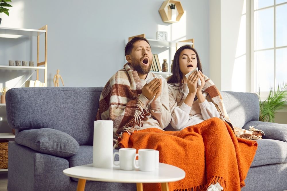 A man and a woman are sitting on a couch wrapped in blankets.