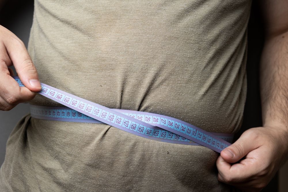 A man is measuring his waist with a tape measure.