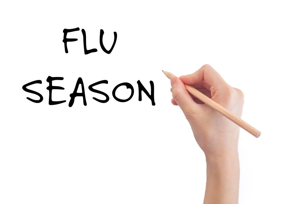 A hand is writing the word flu season with a pencil.