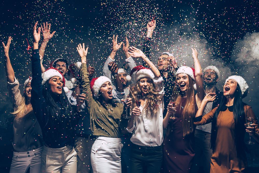 A group of people wearing santa hats are dancing at a christmas party.