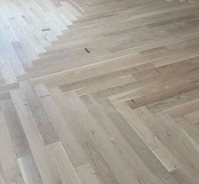Light wood herringbone floor with a small dark speck near the center