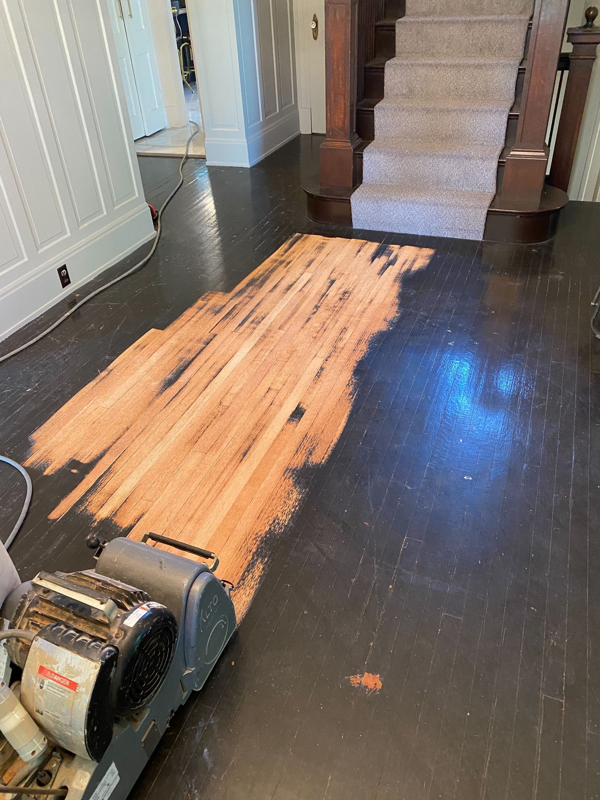 Wood floor being sanded in a hallway with a floor sander and exposed bare wood strip