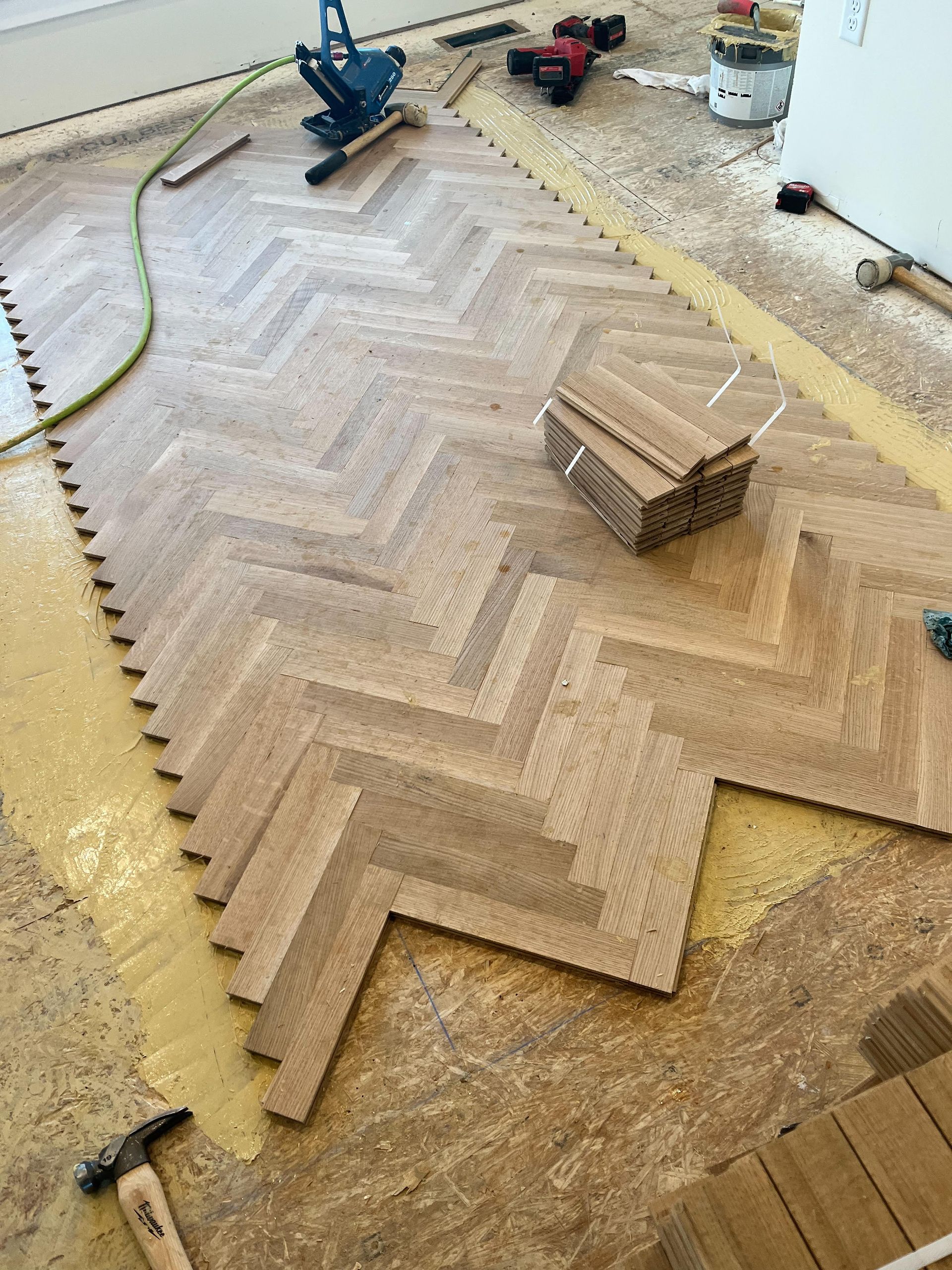 Large herringbone wood floor being installed in a room, with tools and supplies nearby