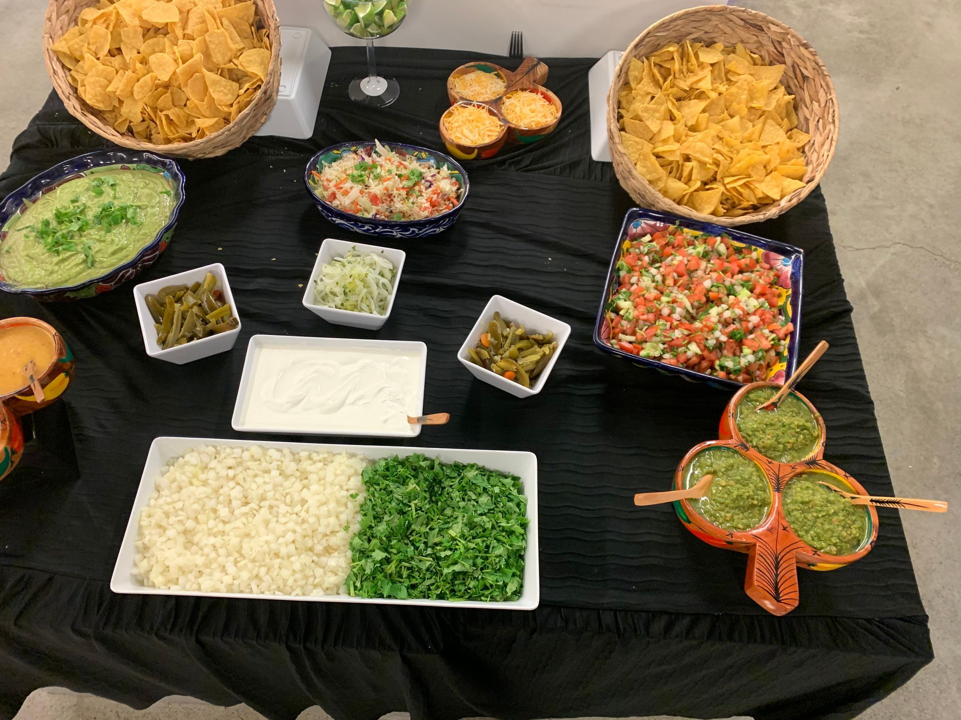 Mexican food buffet with chips, dips, and toppings on a black table.