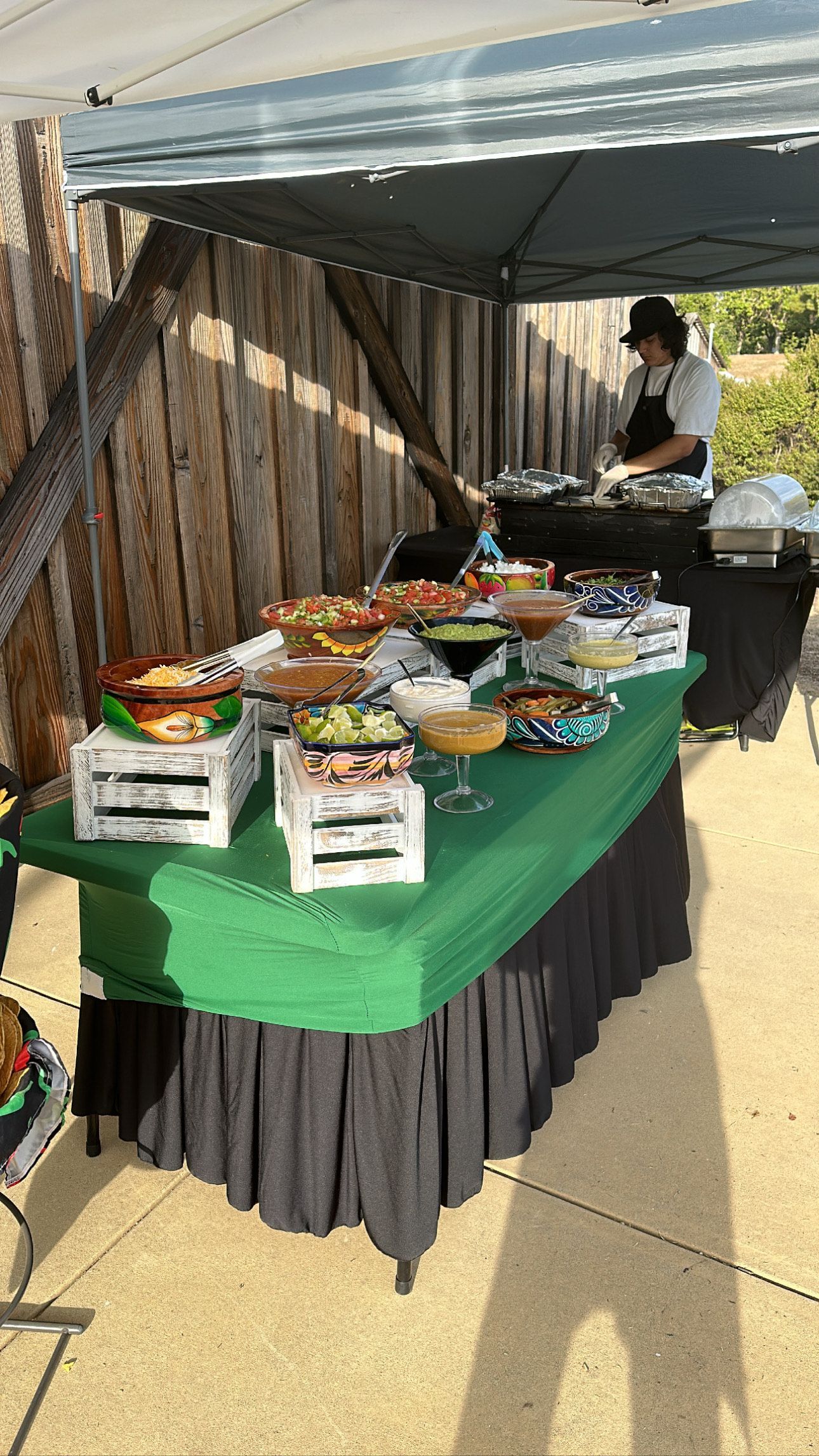 Buffet table with Mexican food, under a tent. A person serves food.