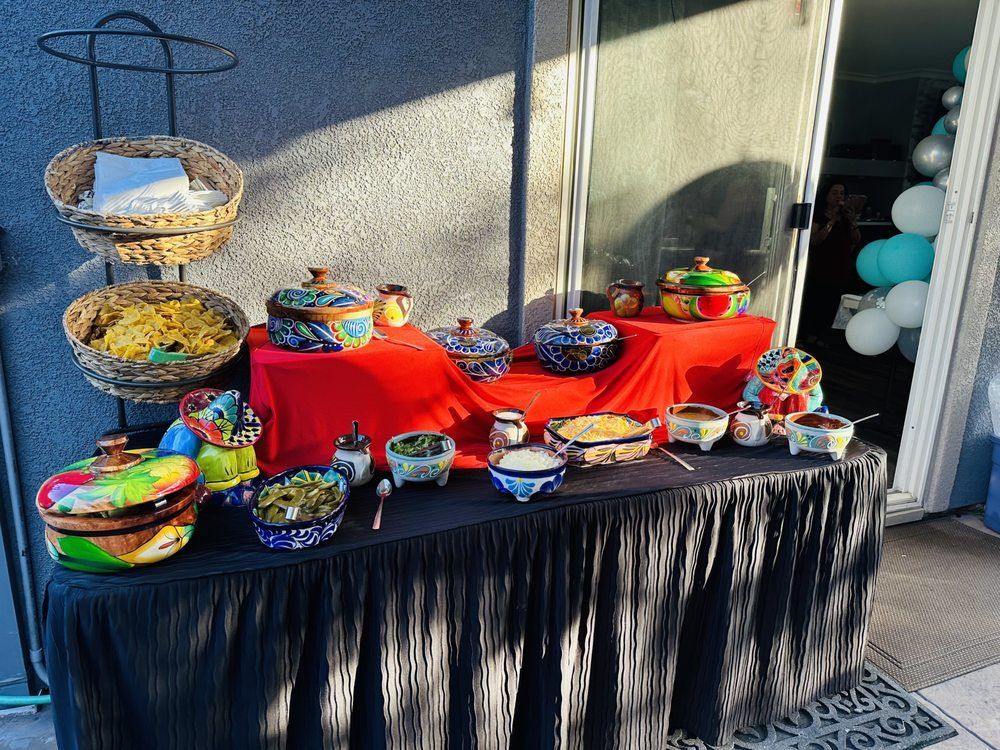 Buffet of Mexican food, colorful bowls, red tablecloth, and decorative serving dishes.
