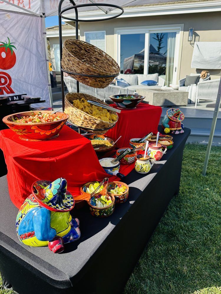 Food buffet outdoors, with colorful dishes and decorations on a black table with red tablecloths.