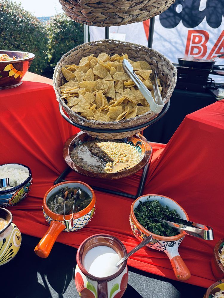 Mexican food buffet: Chips, salsas, and toppings arranged on a red-covered table.