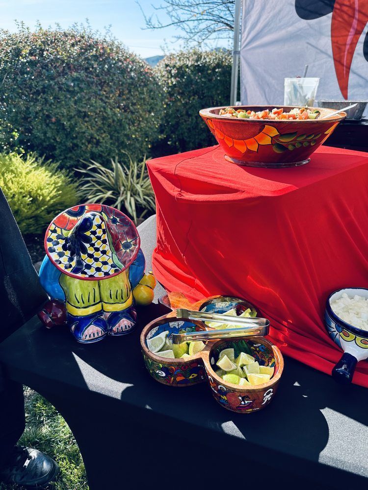 Mexican food setup with colorful bowls of salsa, limes, and a sombrero figure, outdoors.