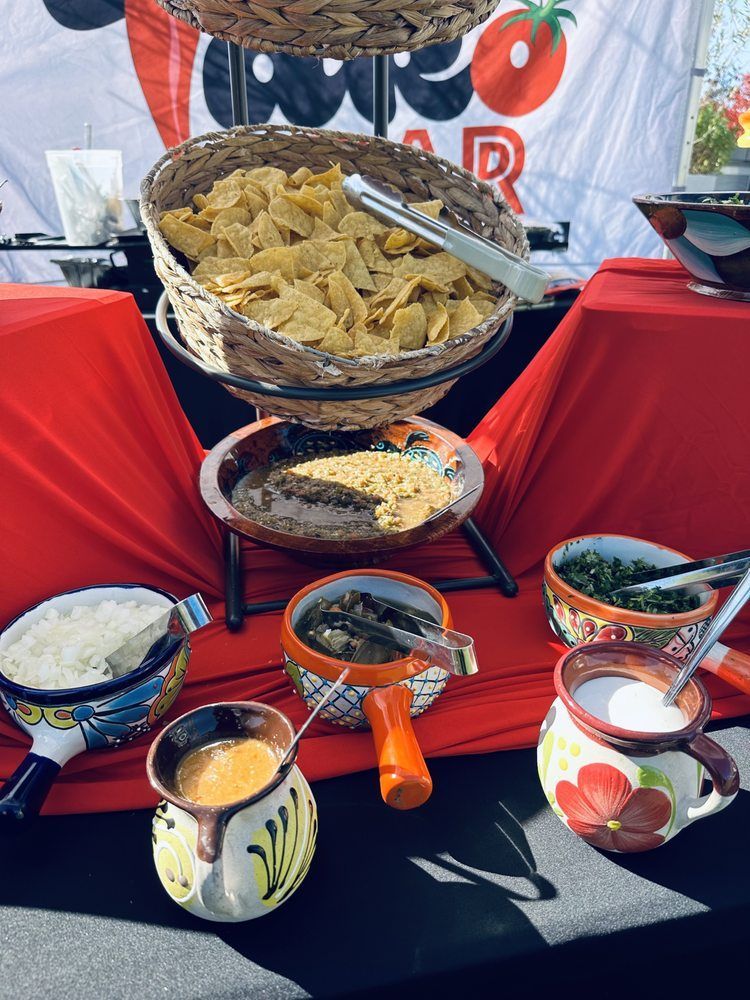 Chips and various dips in colorful bowls at a Mexican food bar, with red tablecloth.