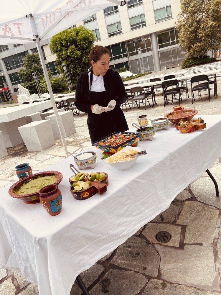 Woman at a table serving food outdoors: guacamole, salsas, and other Mexican dishes.