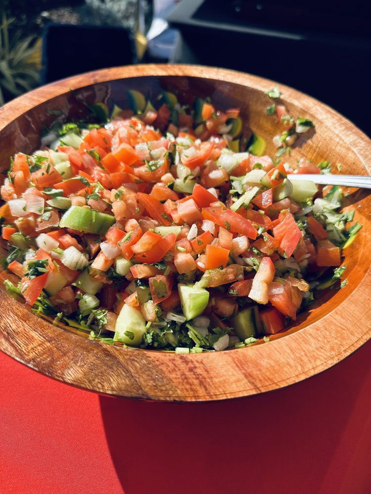 Wooden bowl filled with chopped vegetables: tomatoes, cucumbers, onions.