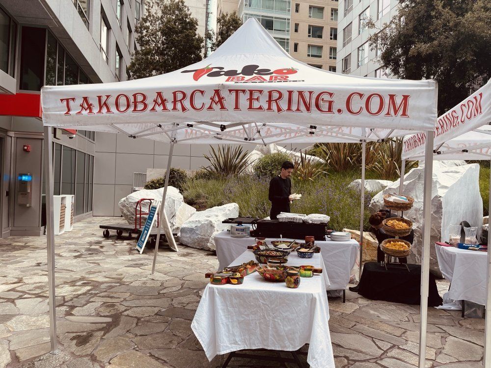 Taco Bar Catering tent setup outdoors with food, server, and website address.