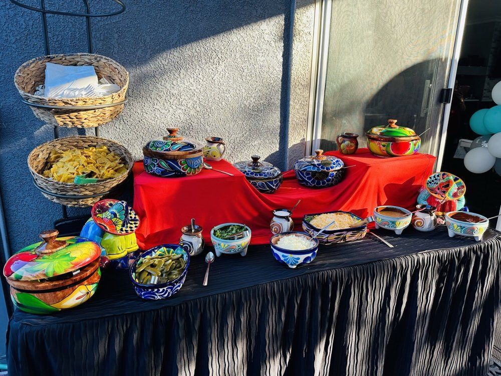 Mexican food buffet with colorful pottery, red tablecloth, and black skirt.