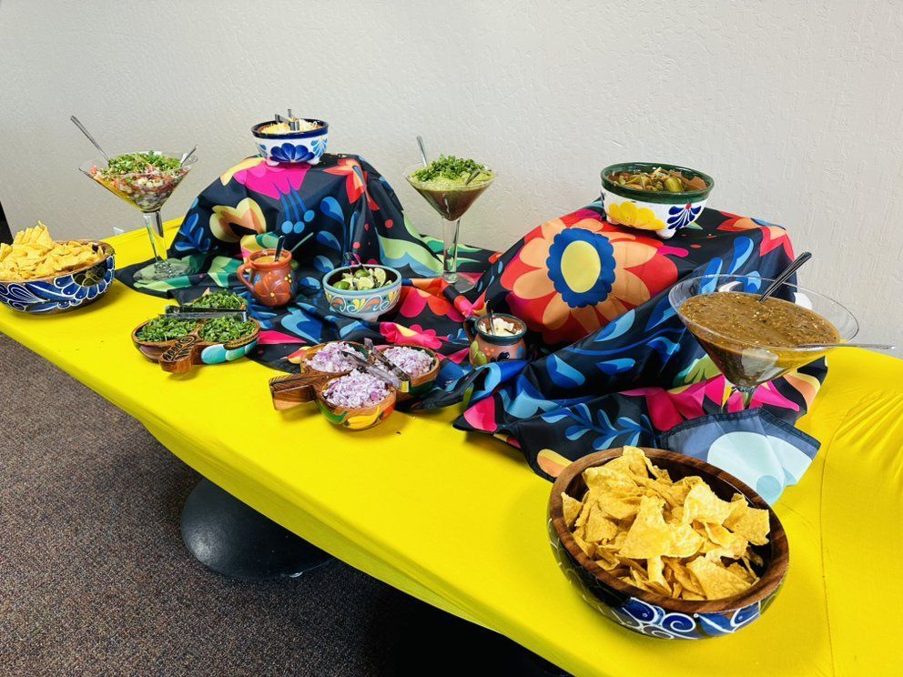 A festive table with Mexican food: dips, chips, salsa, and guacamole, set on a yellow tablecloth, colorful cloth accents.