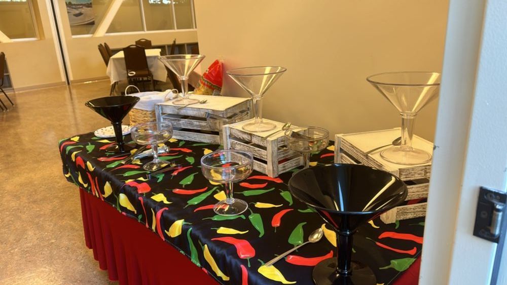A buffet table with martini glasses, a black and red chili pepper tablecloth, and decorative wooden boxes.