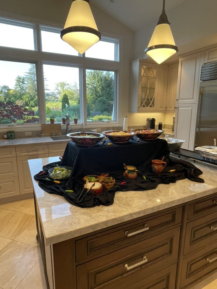 A kitchen island with a black-draped buffet of Mexican food, sunny window in the background.
