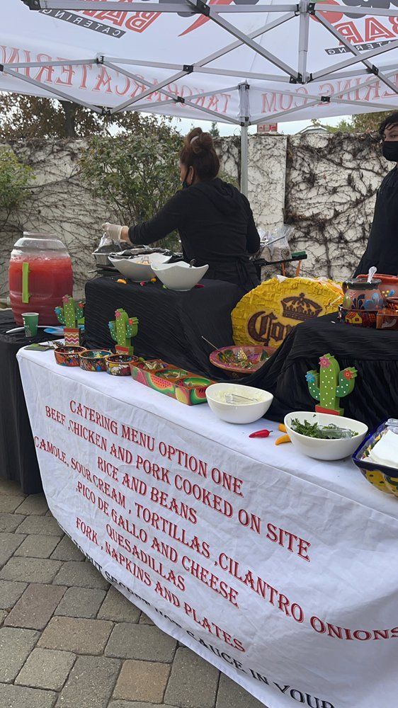 Catering setup with food and staff serving. Includes sign, Corona beer, and cactus decorations.