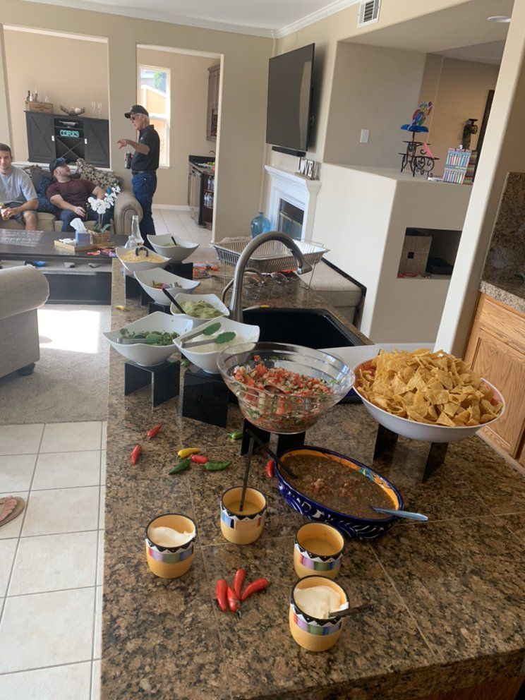 A counter hosts a party spread of salsa, chips, and toppings; people lounge in the background.