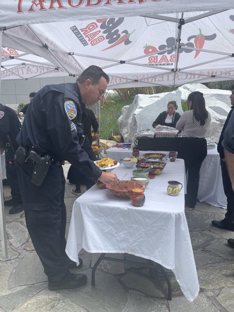 Officer in uniform selects food at a table set up under a tent with a restaurant banner.