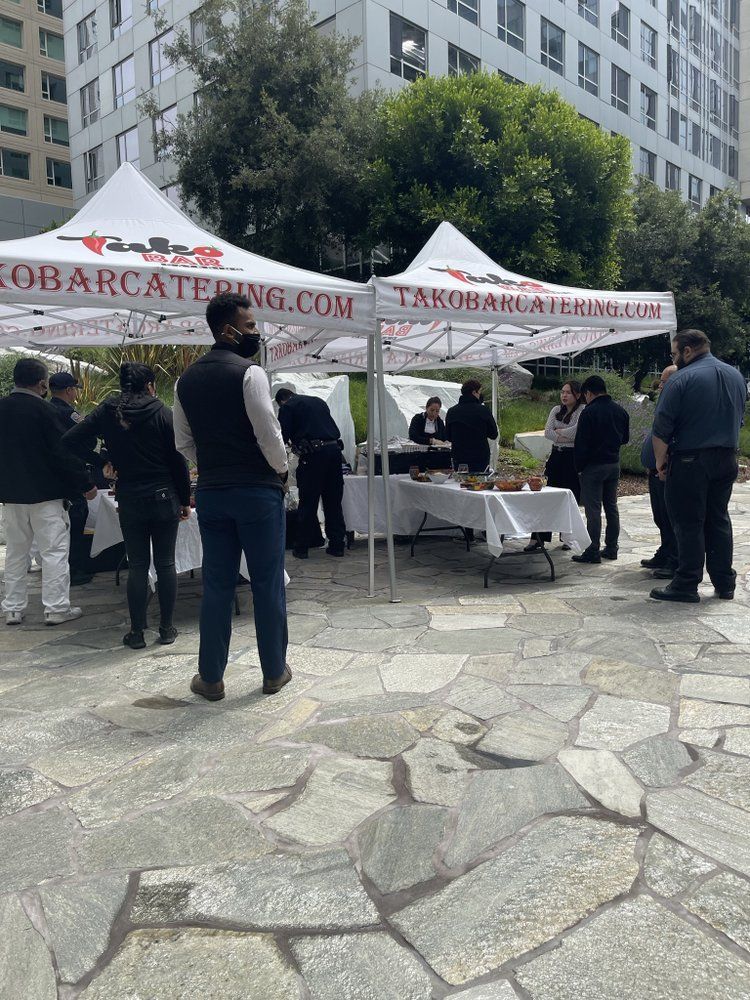 People gathering at a catering tent in a stone park.  A sign says 