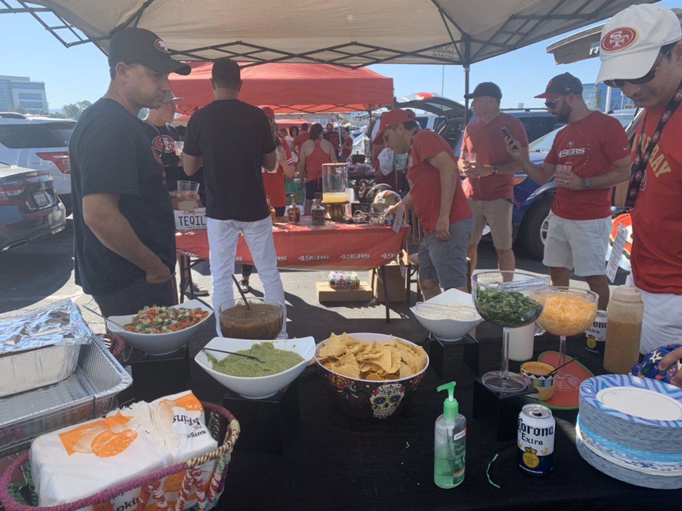 Tailgate party with food, drinks, and people wearing red shirts.