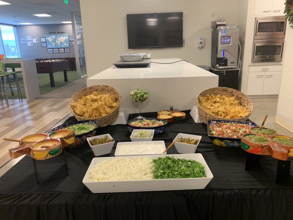 Buffet with Mexican food, including chips, dips, rice, and toppings in an office setting.