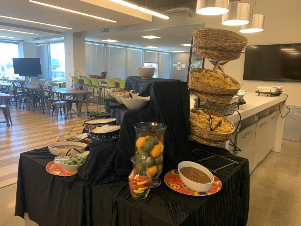 A buffet-style food display in a bright room with tables and a large TV; various dishes and baskets of food.