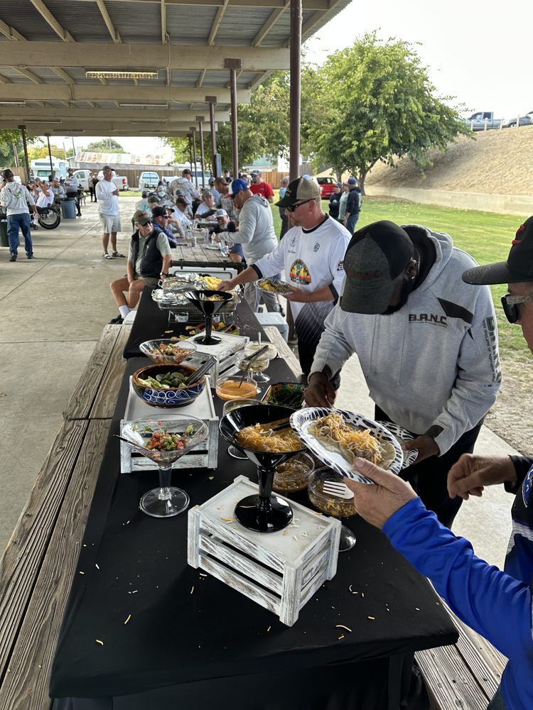 People at a buffet serving food at an outdoor event under a covered shelter.