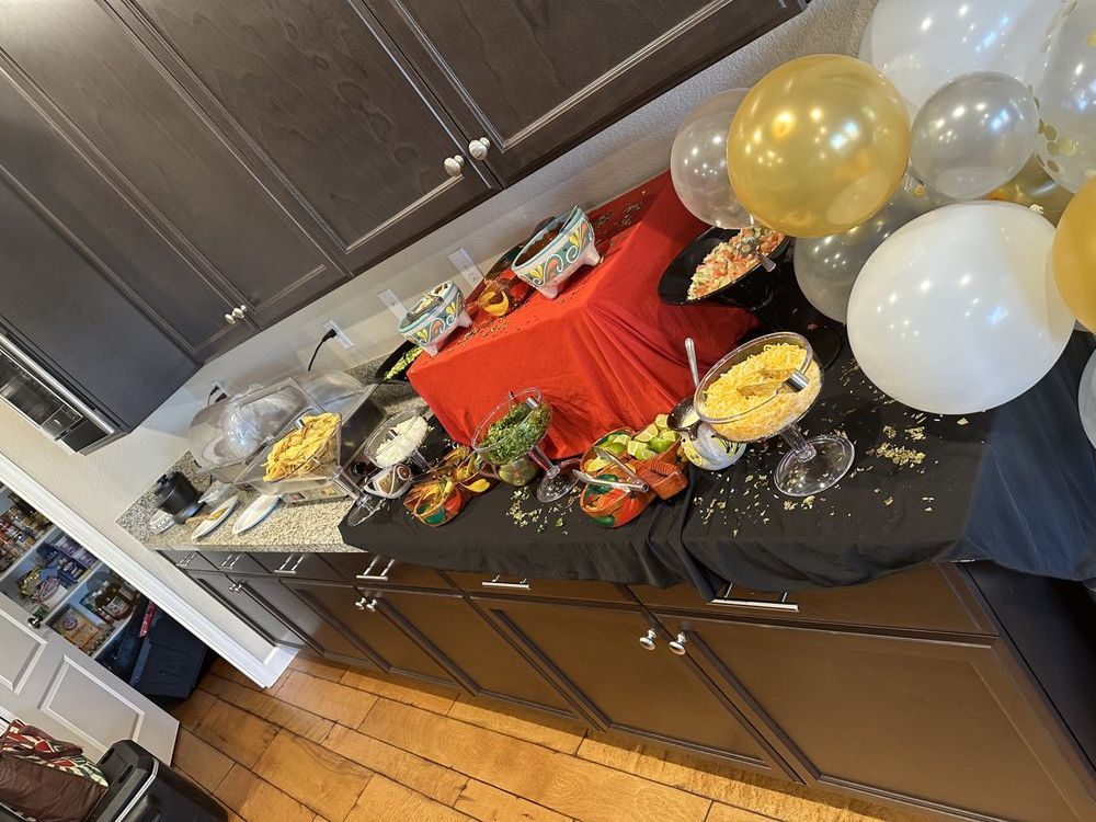 A party buffet on a counter with food, balloons, and red tablecloth.