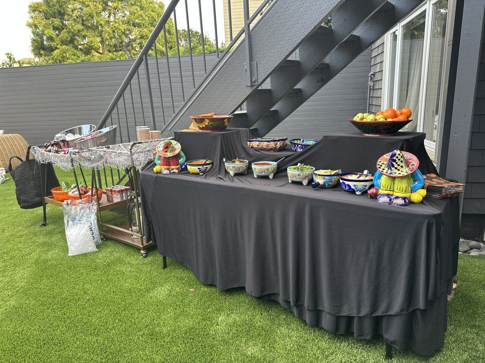 Outdoor food spread on black table with decorative pottery and fruit; staircase in background.