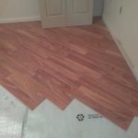 Partially installed red wood-look flooring with white subfloor exposed near a doorway