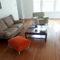 Living room with brown sofa, orange ottoman, green armchair, and glass coffee table on hardwood floor