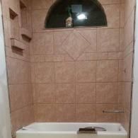 Small tiled bathroom with a white bathtub and arched window above it.