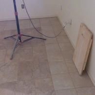 Empty room corner with tiled floor, a light stand, and a wood board leaning against the wall.