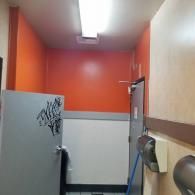 Narrow orange hallway with a gray door and wall-mounted phone under fluorescent light