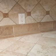 Beige tiled kitchen backsplash and floor with electrical outlet