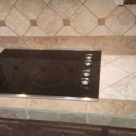 Black built-in stovetop with four control knobs on a tiled kitchen counter